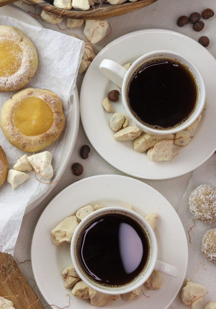 Two cups of baobab coffee with baobab cookies and baobab pulp in the background, made with roasted seeds - one of our favorite baobab recipes.